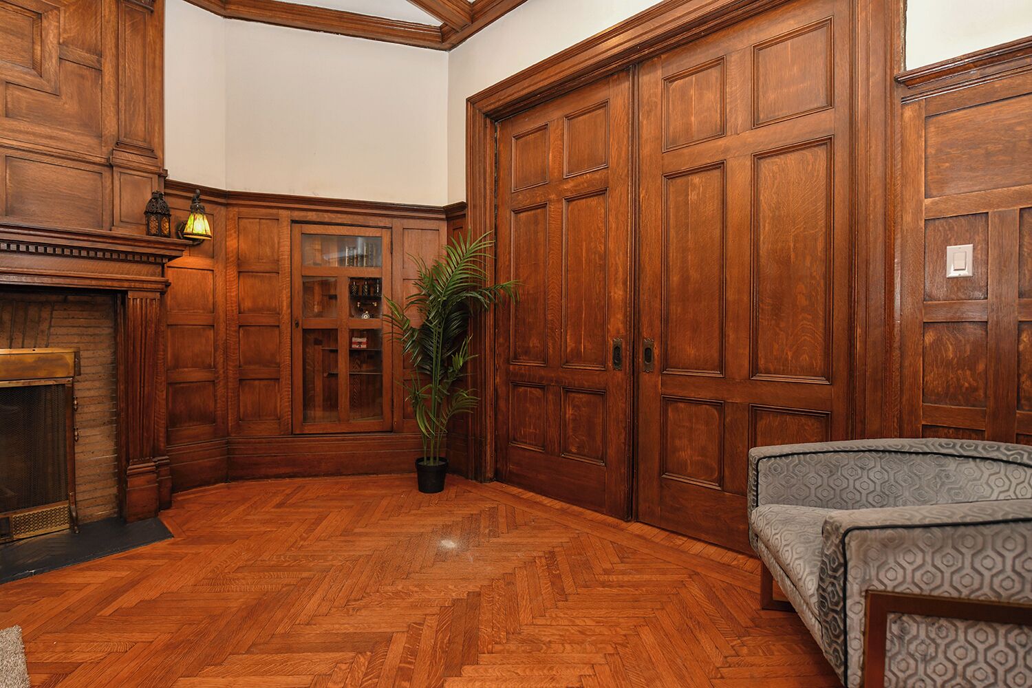 A room with wooden paneling, a fireplace, a large wooden door, and a patterned sofa.
