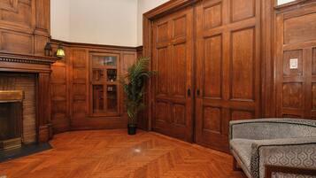 A room with wooden paneling, a fireplace, a large wooden door, and a patterned sofa.