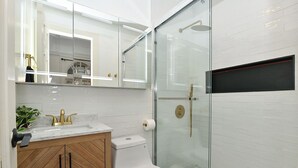 Une salle de bain moderne avec une douche à parois de verre, des toilettes blanches et un meuble-lavabo doté d’un plan de travail en marbre.