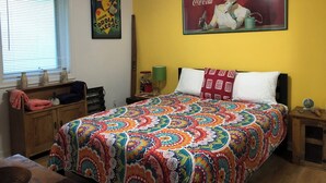 A bedroom with a colorful bedspread, a Coca-Cola poster, and a window with blinds. - Charming 1-bedroom private suite. Easy walk to beach and boardwalk. (Virginia Beach)