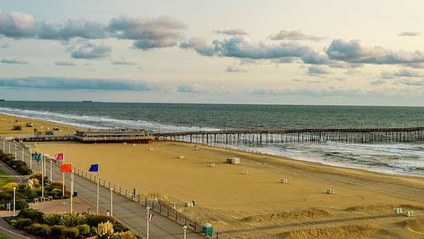 A beach with a wooden pier extending into the ocean, a sandy beach, and a clear sky with clouds. - Charming 1-bedroom private suite. Easy walk to beach and boardwalk. (Virginia Beach)
