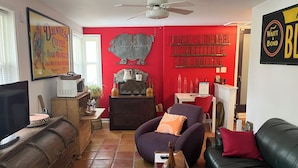 A living room with a red accent wall, a television, a wooden cabinet, a sofa, and a coffee table. - Charming 1-bedroom private suite. Easy walk to beach and boardwalk. (Virginia Beach)