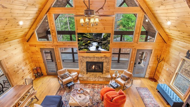 Un vaste espace de vie de style loft, doté d’une cheminée en pierre, de poutres apparentes et de grandes fenêtres donnant sur une forêt.