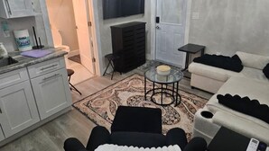 A modern living room with a flat-screen TV, a sofa, a coffee table, and a kitchen area with cabinets and a countertop. - Charming studio in superb Fort Myers that’s conveniently located (Fort Myers)