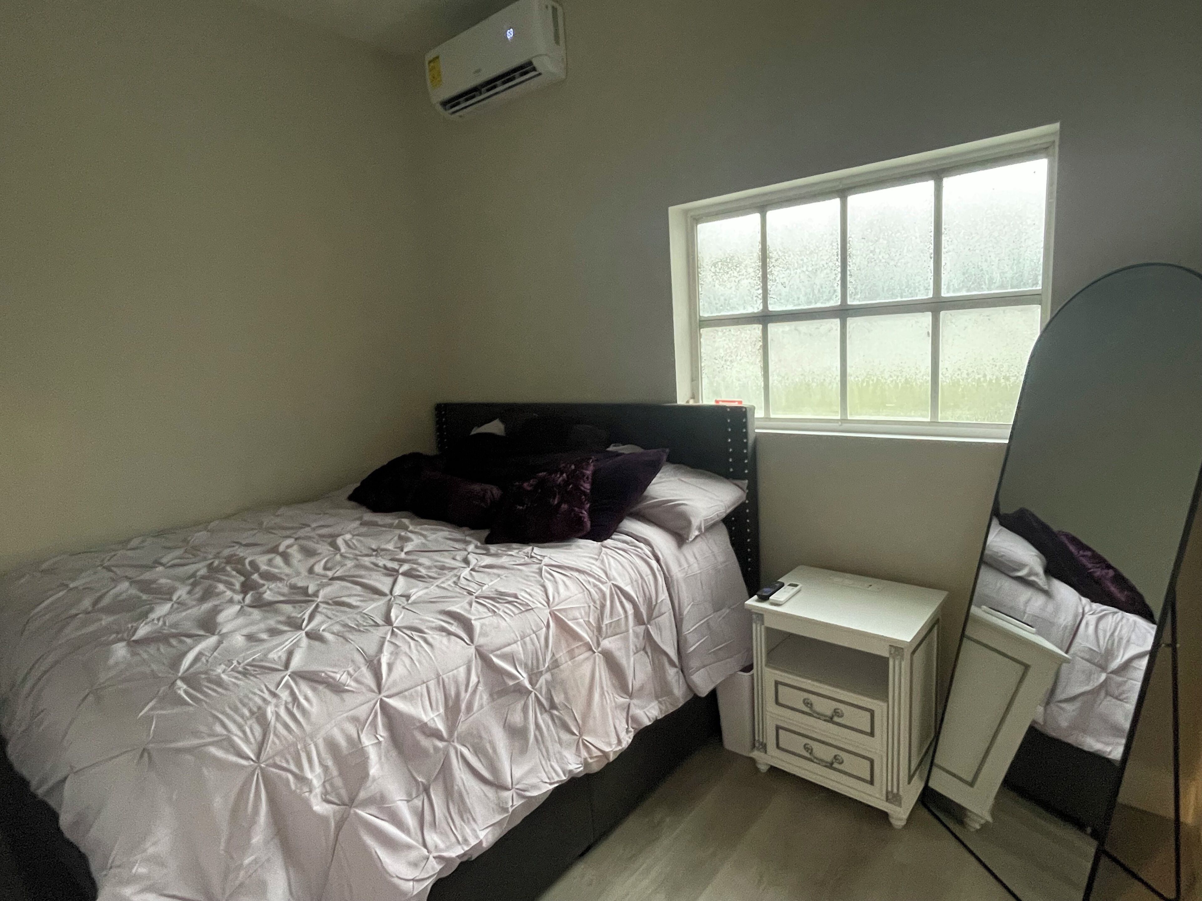 Um quarto com cama, mesa de cabeceira, espelho e janela.