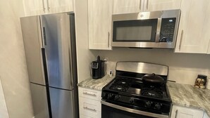 A compact kitchen with a stainless steel refrigerator, a microwave, a stove, and a coffee maker. - Charming studio in superb Fort Myers that’s conveniently located (Fort Myers)