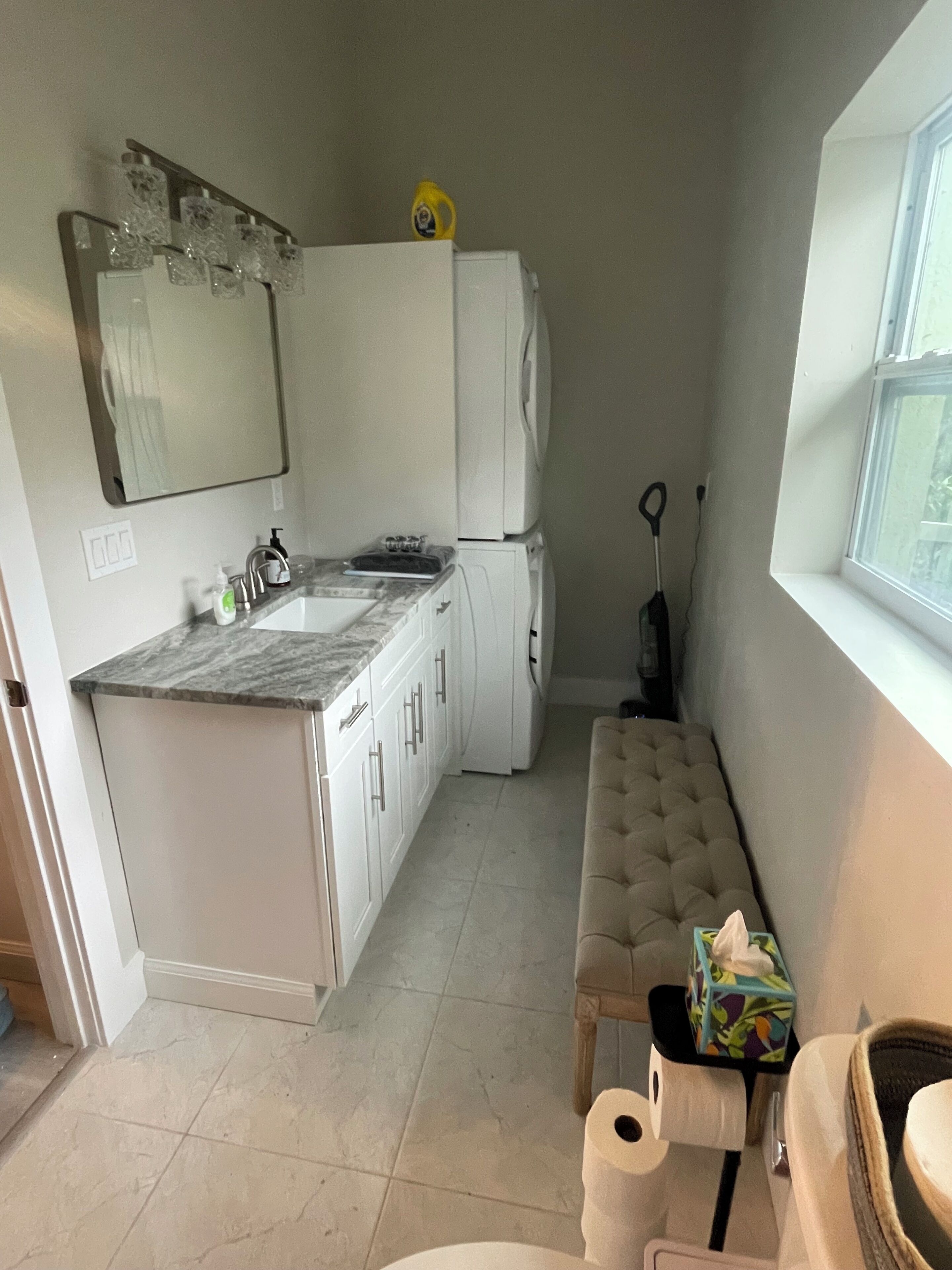 A compact kitchen with a marble countertop, white cabinets, a built-in oven, and a window providing natural light.