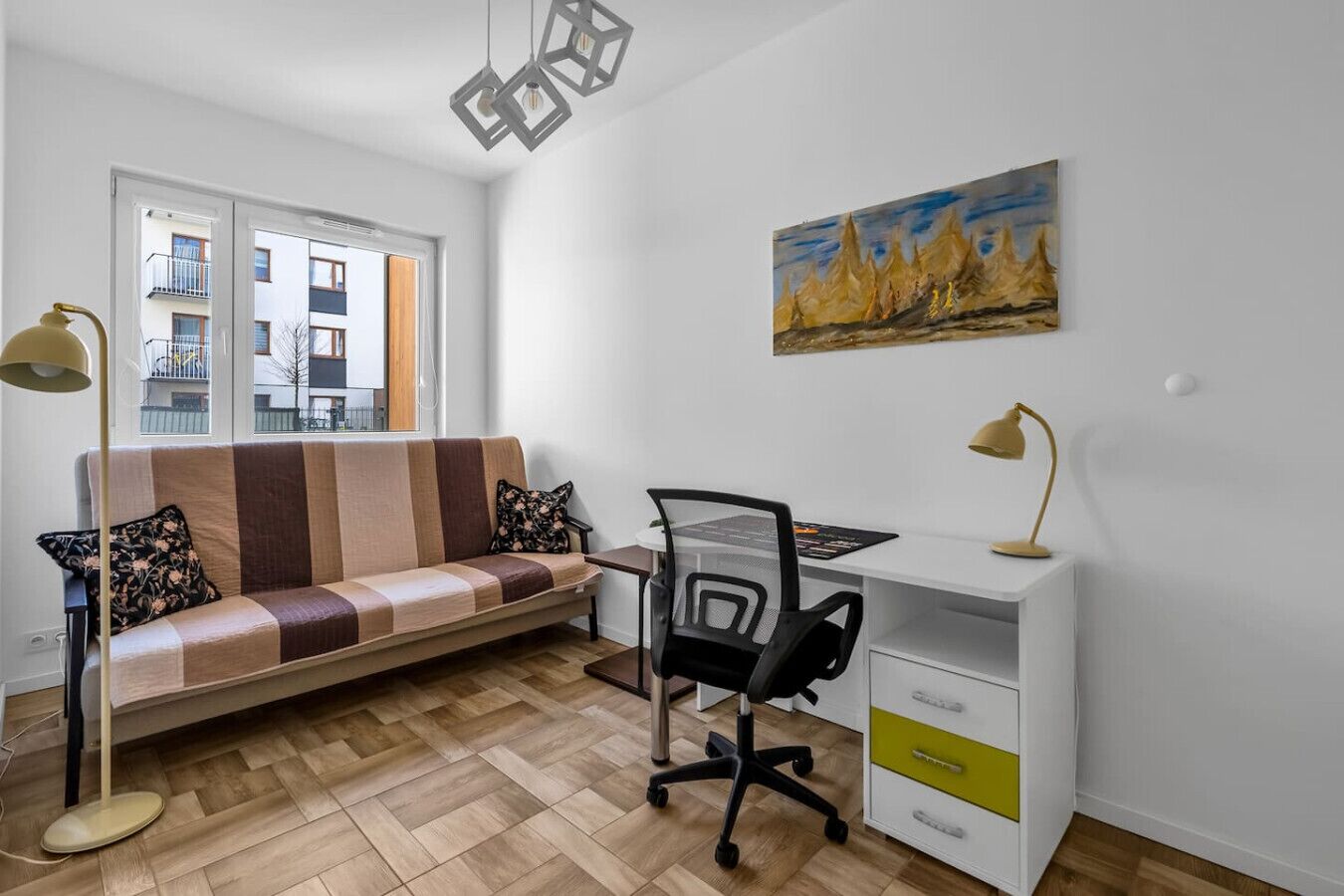 Een modern appartement met een bank, bureau en stoel, een schilderij aan de muur en uitzicht op gebouwen door het raam.