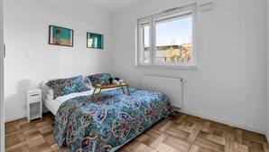 Ein Schlafzimmer mit Bett, Nachttisch, Fenster und Heizkörper.