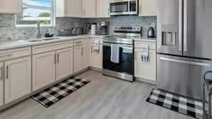 A modern kitchen with light-colored cabinets, stainless steel appliances, and a checkered floor mat. - 4-bedroom house in charming Riviera Beach with WiFi, AC. Relax and unwind (RIVIERA BEACH)