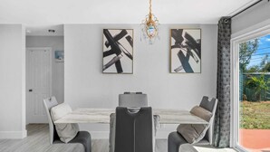 A dining area with a marble table, black and grey chairs, abstract art on the wall, and a chandelier. - 4-bedroom house in charming Riviera Beach with WiFi, AC. Relax and unwind (RIVIERA BEACH)