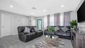A modern living room with two leather sofas, a glass coffee table, and a grey patterned rug. - 4-bedroom house in charming Riviera Beach with WiFi, AC. Relax and unwind (RIVIERA BEACH)