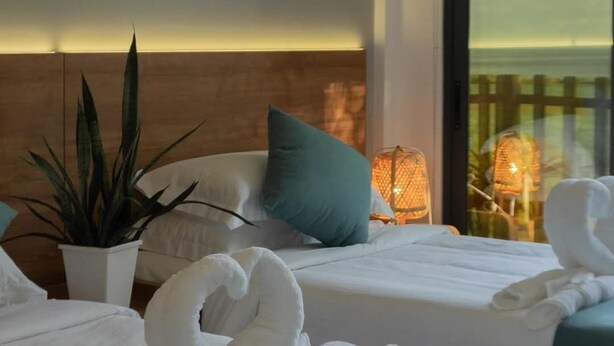 A hotel room with two beds, a potted plant, a nightstand with a lamp, and a view of the sea through large windows. - BAGEECHAA STAY (Dharavandhoo)