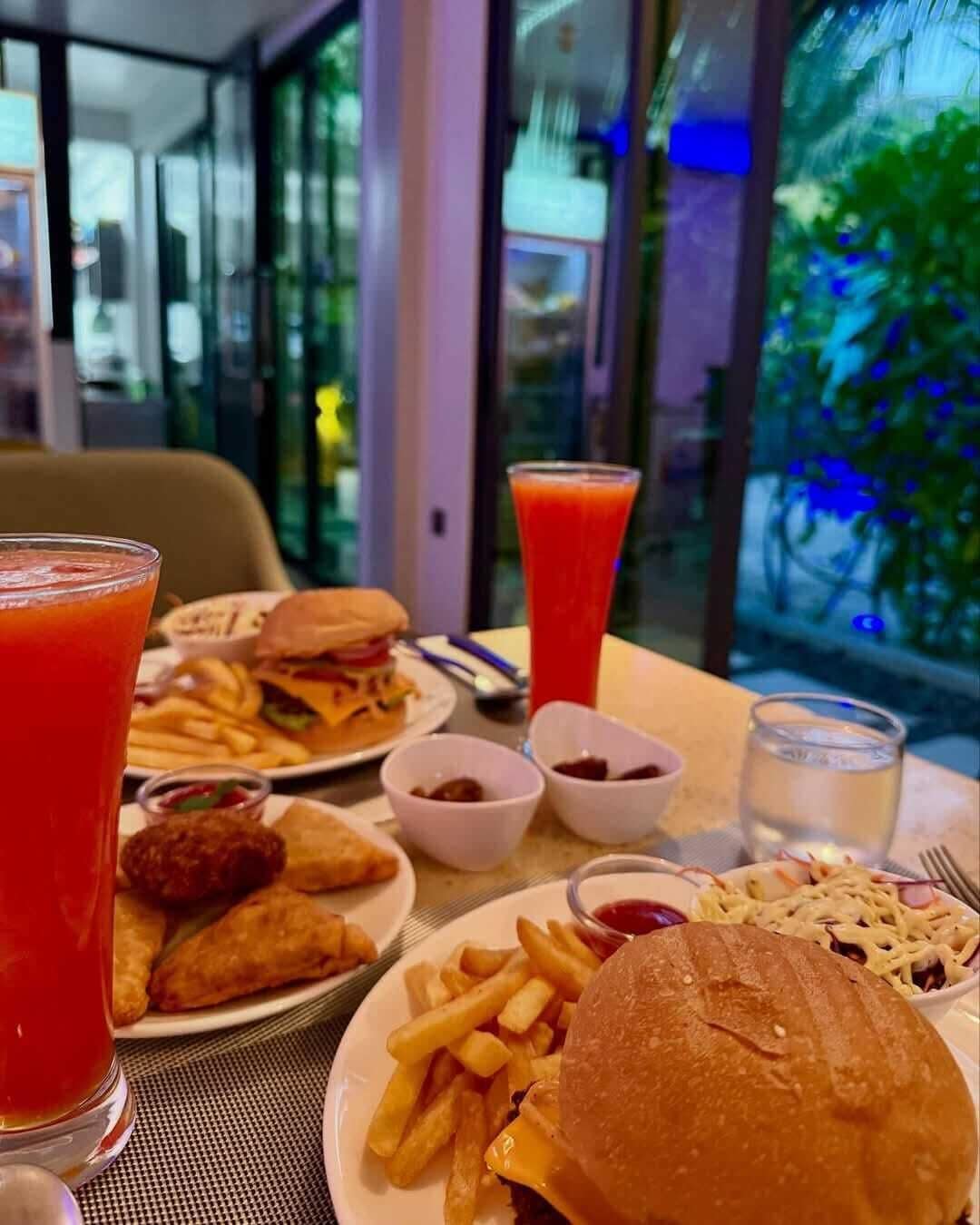 A meal with a burger, fries, and a drink at a table with a view of greenery outside.