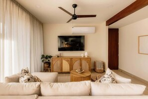 A living room with a sofa, a ceiling fan, a TV, a wooden cabinet, and a plant.