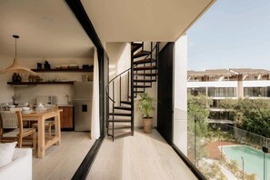 A modern interior with a spiral staircase, a dining area, and a view of a pool and buildings.