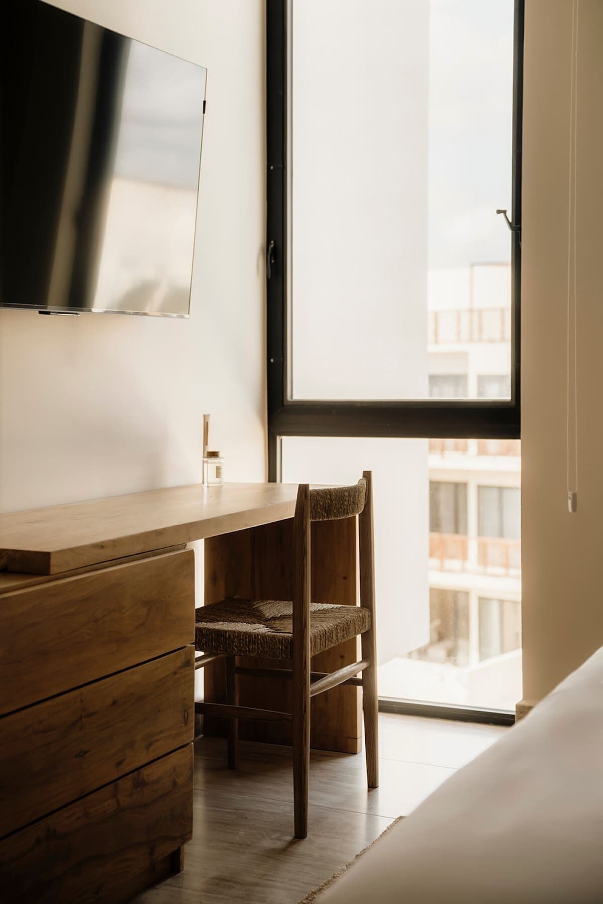 Una habitación con un escritorio de madera, una silla, un televisor en la pared y un ventanal grande.