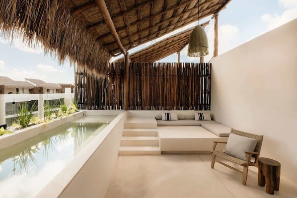 A modern outdoor lounge with a pool, seating area, and a thatched roof.