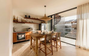 A modern kitchen with wooden cabinets, a dining table with chairs, and a large window with a view of the outdoors.