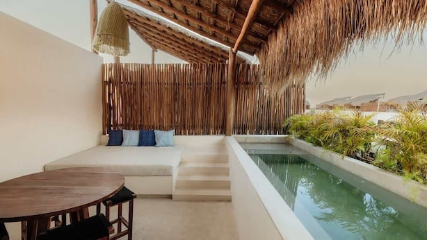 A poolside area with a wooden deck, a seating area with cushions, and a thatched roof structure. - Itzel Samsara Dream Penthouse Beach Club Access (Tulum)