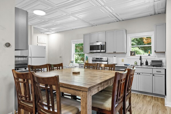 Une cuisine moderne avec des meubles blancs, une table à manger en bois et une grande fenêtre.