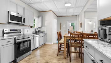 Une cuisine moderne dotée d’appareils électroménagers en acier inoxydable, d’une table à manger en bois et de meubles de rangement blancs.