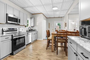 Une cuisine moderne dotée d’appareils électroménagers en acier inoxydable, d’une table à manger en bois et de meubles de rangement blancs.