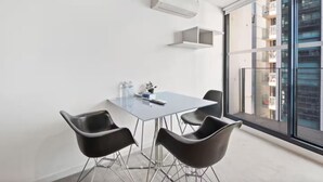 Une pièce moderne avec une table en verre, quatre chaises noires, une petite plante en pot et un distributeur d’eau.