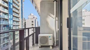 Un balcon doté d’une balustrade en verre, d’un appareil de climatisation et offrant une vue sur les bâtiments voisins.