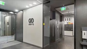 Un intérieur moderne avec une cloison en verre, un logo sur le mur et un espace cuisine à l’arrière-plan.