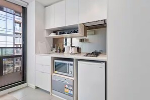 A compact kitchen with white cabinets, a microwave, a small refrigerator, and a coffee maker on the countertop. - Cozy Studio Unit Heart of Melb (Melbourne)