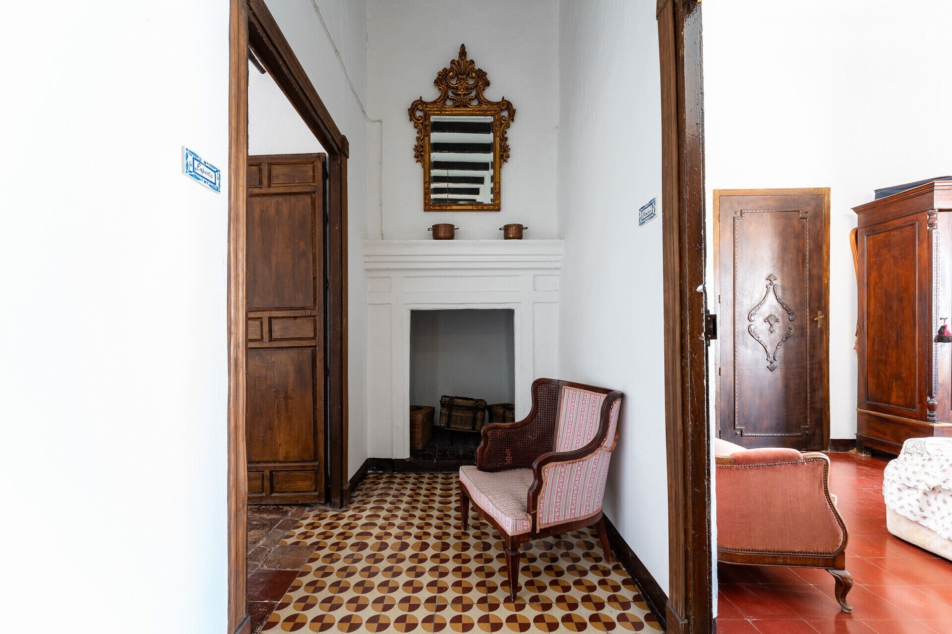 A room with a patterned floor, a fireplace, a wooden door, and a chair.
