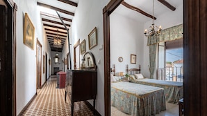 Un couloir au sol décoré de motifs menant à une chambre où se trouvent un lit et une petite table.