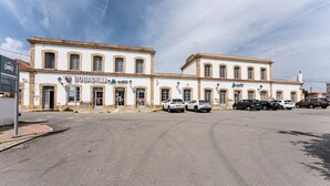 Un immeuble de deux étages avec une façade blanche et de nombreuses fenêtres. Plusieurs voitures sont garées devant, et une enseigne est visible sur le côté gauche.
