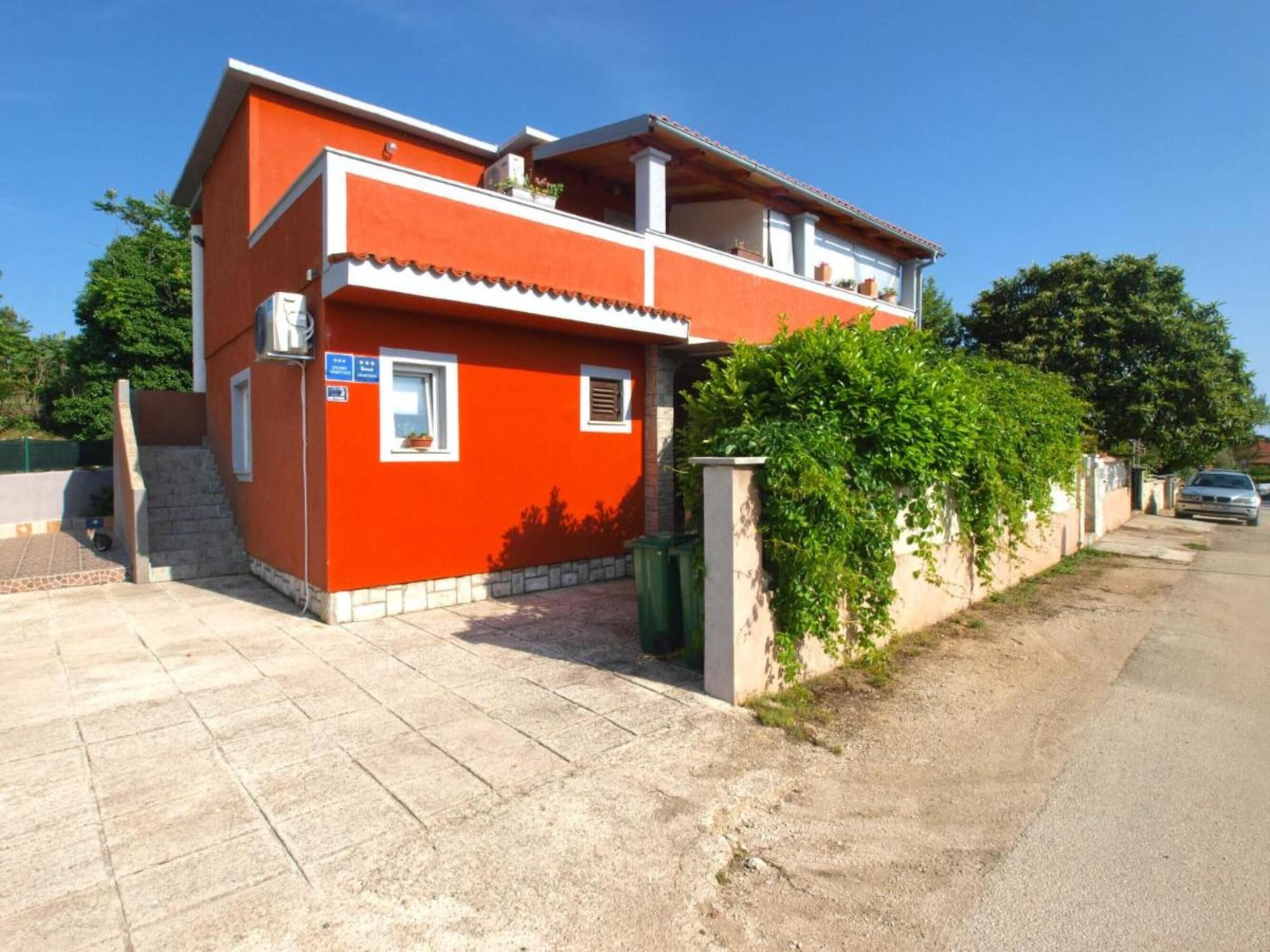 Une maison rouge à deux étages, dotée d’un balcon, d’une petite fenêtre et d’une allée pavée.