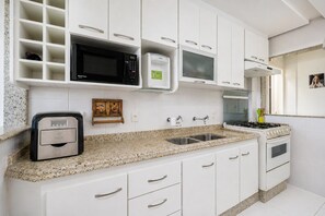 A modern kitchen with white cabinets, a built-in microwave, a coffee machine, a sink, and a stove. - Cf03 Apto vista mar da praia do forte (Cabo Frio)