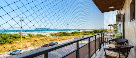 Een balkon met uitzicht op strand en zee, met rieten meubilair en een betegelde vloer.