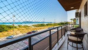 Un balcón con vista a la playa y al océano, que incluye mobiliario de mimbre y piso de baldosas.