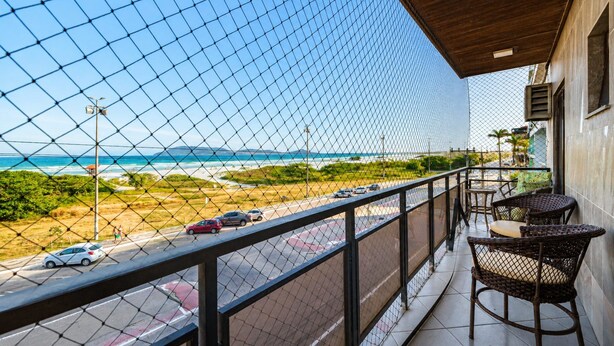 A balcony with a view of the beach and ocean, featuring wicker furniture and a tiled floor. - Cf03 Apto vista mar da praia do forte (Cabo Frio)