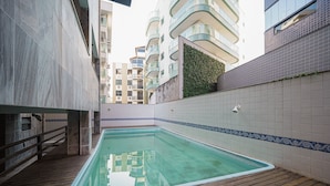 Una piscina con cubierta de madera, rodeada de edificios altos y una pared de azulejos con un borde decorativo.