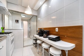 A modern kitchen with a gas stove, coffee maker, and bar stools. - Cf03 Apto vista mar da praia do forte (Cabo Frio)