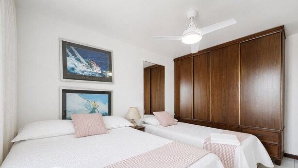 Habitación de hotel con dos camas, ventilador de techo, armario de madera y dos cuadros en la pared.