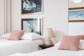A hotel room with two beds, a nightstand, a lamp, and two framed pictures on the wall. - Cf03 Apto vista mar da praia do forte (Cabo Frio)