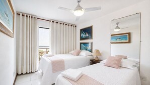 Een hotelkamer met twee bedden, een plafondventilator, een raam met gordijnen en kunstwerken aan de wanden.