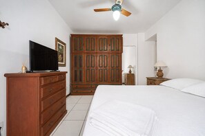 Ein Schlafzimmer mit einem Bett, einem Holzschrank, einem Fernseher auf einer Kommode, einem Deckenventilator und einem Nachttisch mit einer Lampe.