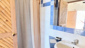 A bathroom with a checkered floor, a wooden door, a striped shower curtain, and a sink with a mirror. - Mancora Beach Hotel  (Máncora)