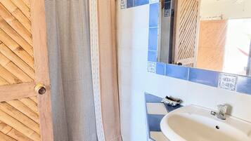 Un baño con suelo a cuadros, puerta de madera, cortina de ducha a rayas y un lavabo con espejo.