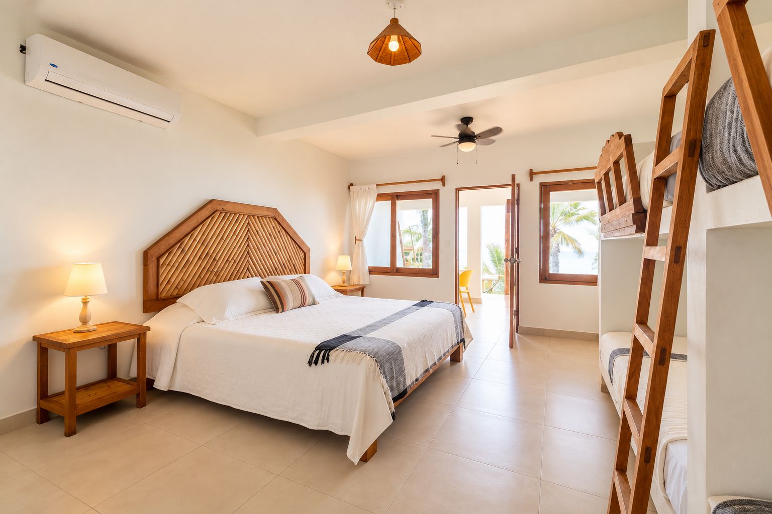 Une chambre à coucher avec un lit, des tables de chevet, un ventilateur de plafond et une vue sur l’extérieur.