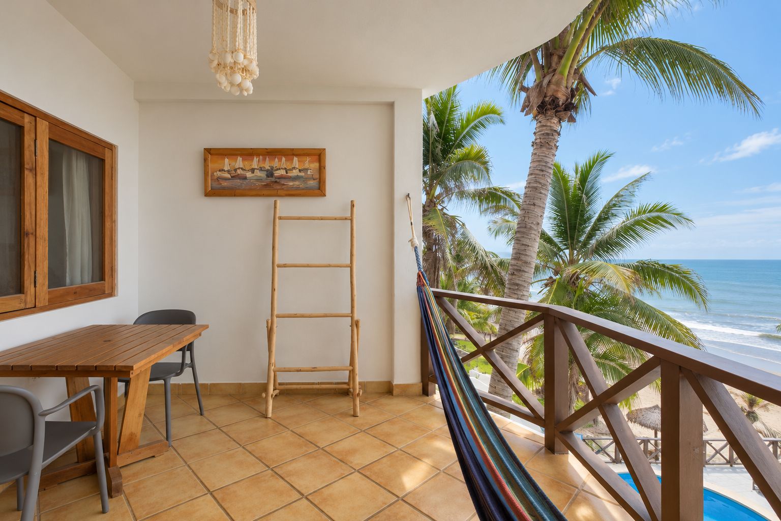 A balcony with a wooden table, chairs, a hammock, and a painting of sailboats.