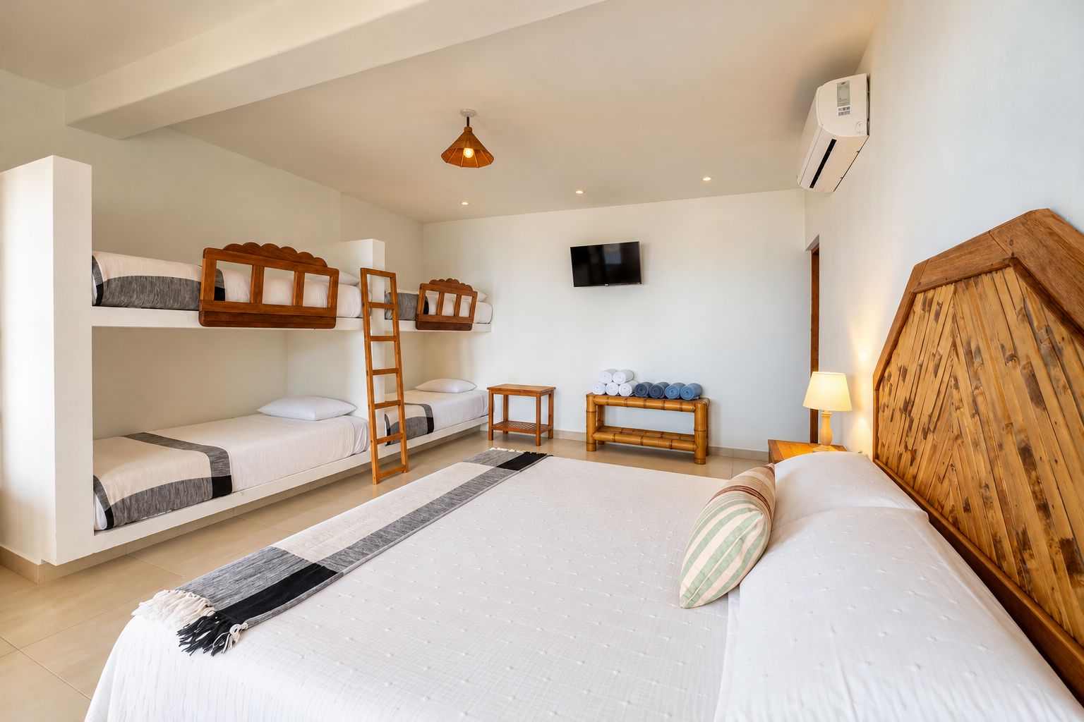 Quarto de hotel com beliches, televisão de tela plana, uma mesinha e um abajur.